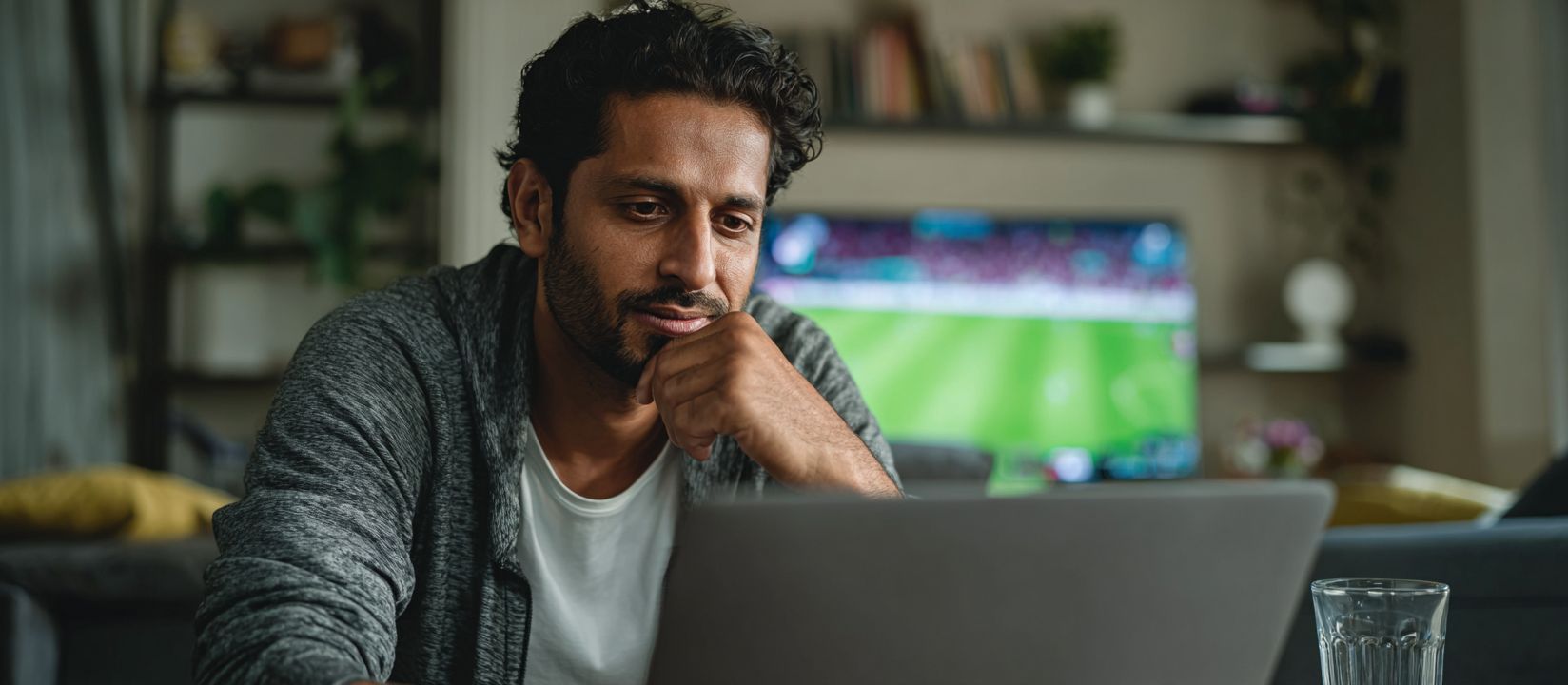 Man watching live football match on TV while using his laptop for BG222 sports betting at home